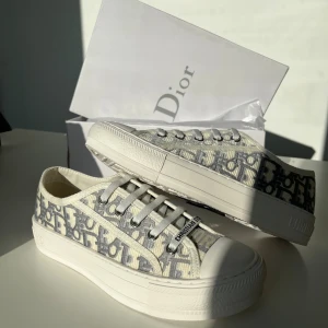 Dior sneakers med monogrammönster - Snygga Dior sneakers med ikoniskt grått och vitt monogrammönster. Låg modell med snörning, platt sula och detaljer som 'CHRISTIAN DIOR' på sidan och hälen. Tillverkade i canvas med gummisula och lyxig insida i skinn. Perfekt för dig som gillar exklusiv streetstyle.