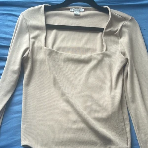 Beige långärmad topp från Amisu - Säljer en stilren beige topp från Amisu med lång ärm och fyrkantig halsringning. Toppen är i ett mjukt, ribbat material som sitter snyggt och har en clean look. Perfekt för dig som gillar minimalistisk stil och neutrala färger.