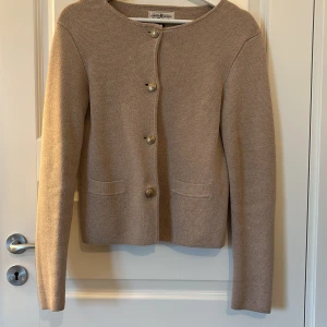 Beige kofta från Hampton Republic - Snygg beige kofta från Hampton Republic med rund hals och dekorativa guldfärgade knappar framtill. Koftan är stickad i mjukt material och har två små fickor fram. ( endast köp via Plick)