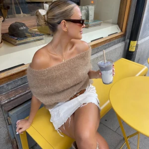 Vinnie Knit design by si - Supermysig beige stickad tröja med offshoulder-design som ger en chill och trendig vibe. Tröjan har en loose passform och är perfekt att styla med jeans eller kjol. Materialet är fluffigt och mjukt, vilket gör den extra skön att bära under svalare dagar.
