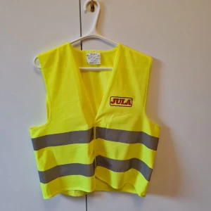 Gul reflexväst från Bluewear XS/S - Reflexväst från Bluewear med Jula-logga, tillverkad i 100% polyester. Västen är knallgul med två breda, horisontella reflexband runt midjan. 