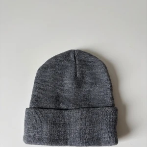 Mörk grå stickad mössa - En enkel och stilren grå stickad mössa med uppvikt kant. Perfekt för kalla dagar och passar till de flesta outfits. Mjuk och bekväm, håller dig varm och ser snygg ut samtidigt. Helt ny.