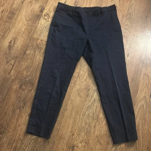 Svarta kostymbyxor med dragkedja - Snygga svarta kostymbyxor med smal passform och diskret dragkedja i sidan. Byxorna har hällor för bälte och bakfickor med minimalistisk design. Perfekta för en clean och stilren look. Vet ej storlek man gissar på L