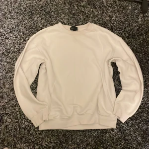Vit loose fit tröja från H&M - En stilren vit sweatshirt från H&M i loose fit-modell. Tröjan har rund halsringning, långa ärmar och ribbade muddar. Perfekt för en avslappnad och clean look. Materialet är mjukt och skönt, troligtvis bomull eller polyester.