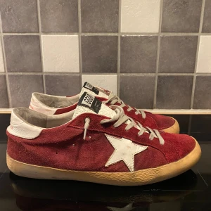 Golden Goose röd - Golden Goose sneakers i röd mocka med vit stjärndetalj. Riktigt snygga och i bra skick, med lite extra fordring som är skönt till hösten. De små ”fläckarna” är designen på dessa skor och inte defekter. Kom med bud eller ställ frågor!