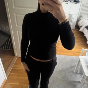 Svart polotröja med lång ärm - Snygg svart polotröja med lång ärm och tight passform. Perfekt för dig som gillar stilrena och enkla plagg. Tröjan har en hög krage och är något croppad, vilket ger en modern look. Passar till både jeans och kostymbyxor.