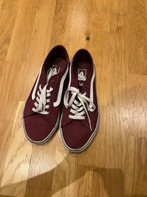 Vinröda Vans, 42,5 - Säljer ett par klassiska Vans sneakers i vinrött med vit sula och vit sidostripes. Använda få gånger men i bra skick!