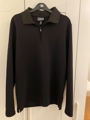  H&M Half zip - Svart pikétröja från H&M med lång ärm och klassisk krage. Tröjan har en half zip-dragkedja framtill och är tillverkad i ett mjukt syntetmaterial som känns skönt mot huden. Passformen är normal och funkar perfekt till jeans eller chinos.