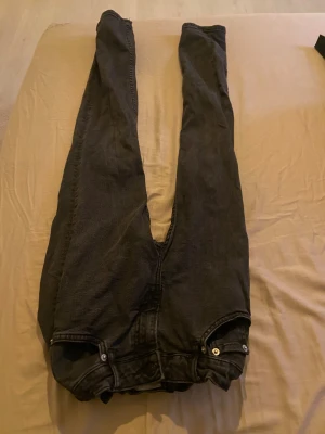 Svarta jeansbyxor med raka ben - Säljer ett par svarta jeansbyxor med klassisk femficksdesign och raka ben. Byxorna har knapp och dragkedja framtill samt silverfärgade nitar vid fickorna. Perfekt för dig som gillar en enkel och tidlös stil.