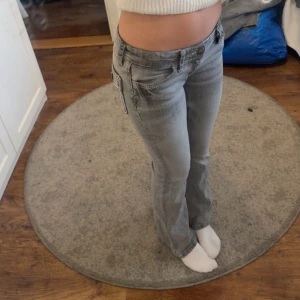 Grå lågmidjade bootcut jeans med fickdetaljer - Ett par skitsnygga grå bootcut jeans, lågmidjade. De har en snygg design på baksidan. Dessa passar verkligen till allt. 