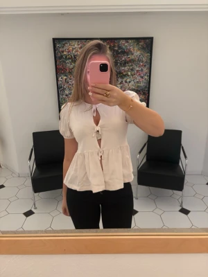 Ljusrosa blus med knyt och puffärm - Supersöt ljusrosa blus från Gina Young med tre knyt framtill och puffiga korta ärmar. Blusen har en rund halsringning och volang nedtill som ger en flowy känsla. Storlek 170 men sitter som S💕