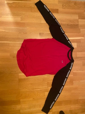Röd och svart långärmad tröja Hollister - Säljer en snygg långärmad tröja från Hollister i storlek S. Tröjan har röd kropp och svarta ärmar med Hollister-tryck längs ärmarna. Klassisk logga på bröstet och rund hals. Tillverkad i mjuk bomull, perfekt för chill dagar.