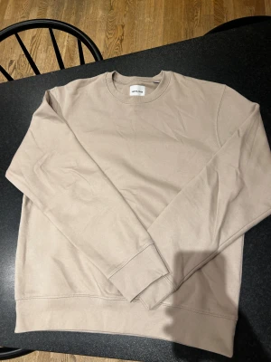 Beige sweatshirt från Jack & Jones - Säljer en stilren beige sweatshirt från Jack & Jones. Tröjan har rund hals, långa ärmar och är tillverkad i mjuk bomull. Perfekt för dig som gillar enkel och clean stil. Passar lika bra till jeans som till mjukisbyxor. Använt den ca 3 gånger.