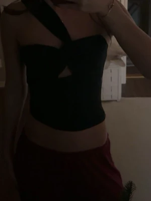 Svart omlott topp - Säljer en svart topp med omlott-detalj och breda axelband som korsas framtill. Toppen har en snygg cut-out vid bröstet och är croppad i modellen. Materialet är mjukt och stretchigt. 