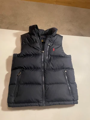 Svart dunväst från Polo Ralph Lauren - Säljer en svart dunväst från Polo Ralph Lauren. Storlek 140. Vill ha runt 600 för den men kan också gå ner lite i pris. Om ni har några frågor är de ba att skriva👍