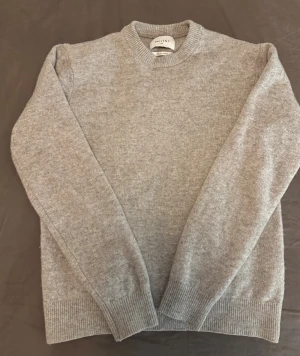 Grå merinoulltröja från Vailent XS - Snygg grå stickad tröja från Vailent i mjuk merinoull. Rund halsringning och ribbade muddar vid ärmslut och nederkant. Perfekt för dig som gillar enkel och stilren design med skön passform. Storlek XS.