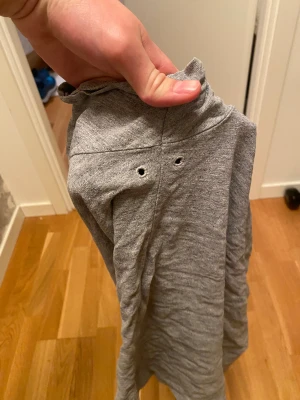 Grå t-shirt från Superdry med ficka - Säljer en grå t-shirt från Superdry med en bröstficka som har en orange detalj och en svart Superdry Surplus Goods-etikett. T-shirten är kortärmad och har en klassisk passform. Materialet känns mjukt och är troligen bomull, perfekt för chill dagar.