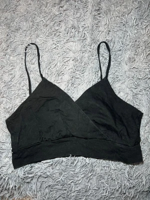 Svart omlott linnetopp med smala band - Säljer en svart omlott linnetopp med smala axelband. Toppen är croppad och har en enkel, stilren design. Materialet består av 95% bomull och 5% elastan vilket gör den mjuk och stretchig. Perfekt att styla med jeans eller kjol för en chill look. Det står ingen storlek men skulle säga L/XL