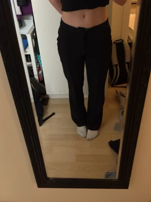 Svarta kostymbyxor med rak passform - Säljer ett par svarta kostymbyxor med rak och lite loose passform. Byxorna är mellan midjade och har en klassisk dragkedja men kampen är borta så jag har satt dit en säkerhetsnål och det funkar lika bra 😊 Materialet känns som polyester och de har fickor på sidorna. Fråga mig om ni undrar något❤️