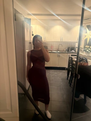 Vinröd glittrig meshklänning - Säljer en vinröd långklänning med glittriga detaljer och meshpartier. Klänningen är ärmlös och har en figurnära passform med markerad byst och transparenta partier upptill. Perfekt för dig som vill sticka ut med en elegant och trendig look. Ny med prislapp 