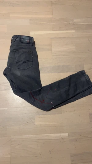 Replay anbass - Svarta jeans från Replay med slim passform och slitna detaljer på framsidan. Jeansen har röda och vita färgstänk som ger en cool och unik look. Perfekt för dig som vill ha ett par unika replay jeans.