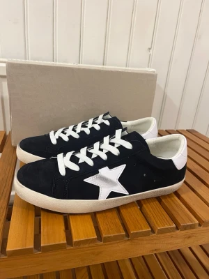 Golden Goose skor - Snygga marin blåa sneakers från Golden Goose med vit stjärndetalj på sidan och vit hälkappa med logga. Skorna har vita snören och en platt sula. Ovandelen är i mocka och detaljer i skinn, väldigt bra skick storlek 43