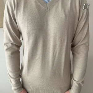  v-ringad kashmir tröja - En stilren beige kashmir tröja med v-ringning och långa ärmar. Tröjan har en klassisk passform och ribbade muddar vid ärmslut och nederkant. Perfekt för lager-på-lager och funkar året runt.