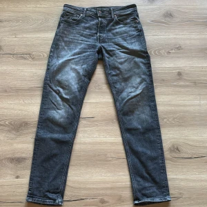 Mörkgrå tapered jeans från Jack & Jones - Snygga mörkgrå jeans från Jack & Jones i modellen Tapered/Mike. Jeansen har en tvättad look med ljusare partier och klassisk femficksdesign. De är tillverkade i bomull och polyester och har en tapered passform som smalnar av nedtill.