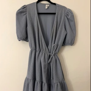 Ljusblå omlottklänning & Other Stories - Ljusblå omlottklänning från & Other stories med puffärmar, knyt i midjan och volangdetaljer. Klänningen har ribbad struktur och v-ringning. Använd 1-2 gånger.