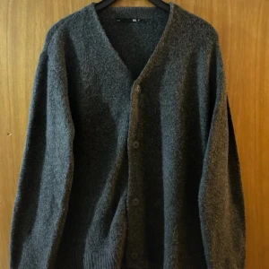 Mörkgrå kofta, storlek M - Mysig mörkgrå kofta från Lager 157 i storlek M. Koftan är stickad med en lite luddig yta, har v-ringning och knäpps med fyra knappar framtill. Perfekt för lager-på-lager och chill dagar. Långärmad och med ribbade muddar vid ärmslut och nederkant.