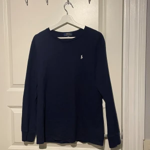 Marinblå långärmad tröja Polo Ralph Lauren - Snygg marinblå långärmad tröja från Polo Ralph Lauren i storlek XL i barnstorlek, som liknar S i herrstorlek. Tröjan har rund hals och klassisk broderad logga i vitt på bröstet. Tillverkad i mjuk bomull som är skön mot huden och passar perfekt till jeans eller chinos.