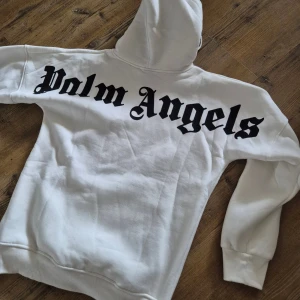 Vit hoodie med tryck - Snygg vit hoodie från med stor svart logga över ryggen och mindre logga framtill. Klassisk känguruficka, huva med snörning och ribbade muddar. Perfekt för dig som gillar streetwear och vill sticka ut med en clean look.