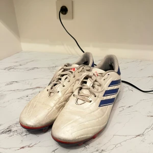 Adidas Copa vita storlek 44 - Säljer ett par Adidas Copa fotbollsskor i vitt med blå detaljer och röda dobbar. Skorna har klassisk snörning och är tillverkade i syntetmaterial. Perfekta för dig som vill sticka ut på planen med stilrena och sportiga skor. Finns lite slitage vid hälen men funkar bra. Det är storlek 44.