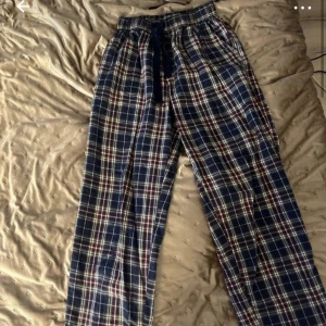 Rutiga mjukisbyxor med snörning - Mysiga mjukisbyxor i blått med röd och vit rutig design. Byxorna har resår i midjan och snörning för extra komfort. Perfekta för chill dagar hemma eller som pyjamasbyxor.