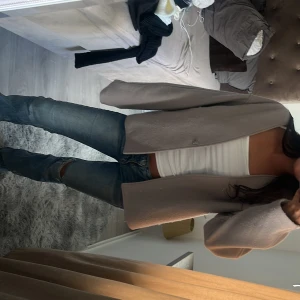 Beige/ grå jacka från Kappahl - Stilren beige höst jacka från Kappahl i ullblandning. Västen har en rak och loose passform med v-ringad hals och enkel knäppning framtill. Perfekt att slänga över en topp för en clean och trendig look. Den e helt slutsåld på hemsidan 