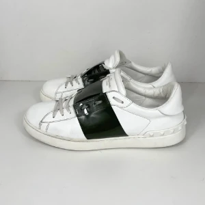 Valentino Garavani Open sneakers vit/grön - Snygga Valentino Garavani Open sneakers i vitt skinn med grön glansig  över vristen. Klassisk rund tå, platt sula och coola nitar baktill på hälen. Perfekta för dig som gillar stilrena men ändå unika sneakers. 7300 kostar dom nya skick 9/10