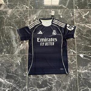 Real Madrid marinblå matchtröja Adidas - Snygg Real Madrid fotbollströja i marinblått med tunna ränder, vita Adidas-ränder på axlarna och HP-logga på ärmen. Tröjan har rund hals, korta ärmar och vita detaljer längs sidorna. Materialet är lätt och andas, perfekt för träning eller match.