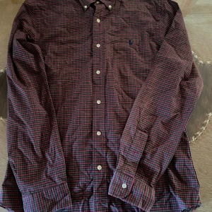 Rutig skjorta Polo Ralph Lauren M - Säljer en rutig skjorta från Polo Ralph Lauren i slim fit-modell. Skjortan har röda, gröna och svarta rutor, klassisk krage och knäppning framtill. Tillverkad i stretchig bomull för extra komfort. Perfekt för dig som gillar en stilren och tidlös look.