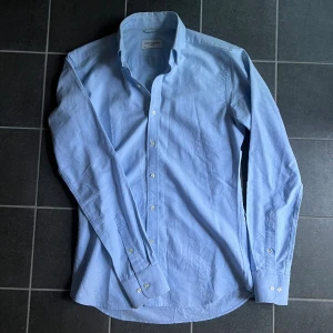 Ljusblå skjorta från John Henric - Snygg ljusblå skjorta från John Henric i klassisk modell med lång ärm och knappar framtill. Skjortan är tillverkad i bomull och har en stilren krage. Perfekt för dig som gillar en clean och fräsch look. Storlek 37, sitter som S!