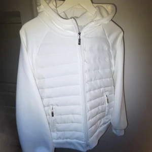 Vit pufferjacka med huva  - Snygg vit cardigan med huva och dragkedja framtill. Jackan har quiltade paneler på både fram- och baksida, två fickor med dragkedja och en clean look. Perfekt för dig som gillar stilren och sportig vibe. Perfekt till hösten. Pris kan diskuteras. Kolla gärna min profil för mer.