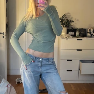 Ljusgrön ribbad croppad tröja - Snygg ljusgrön croppad tröja med ribbad struktur och lång ärm. Tröjan har en figurnära passform och v-ringad halsringning, perfekt för dig som gillar en enkel men trendig stil.