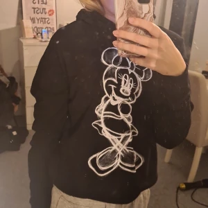 Svart hoodie med Minnie Mouse-tryck - Svart hoodie från Disney med stor vit skissad Minnie Mouse på framsidan. Tröjan har huva och långa ärmar, perfekt för dig som gillar en chill och lekfull stil. Mjuk insida och klassisk passform. Snygg detalj för dig som älskar Disney!