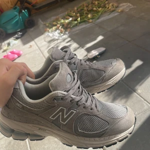 Grå New Balance 2002R sneakers - Säljer ett par grå New Balance 2002R sneakers i storlek 40.5. Skorna har meshpaneler och mockadetaljer, klassisk N-logga på sidan och snörning framtill. Snygg chunky sula och riktigt bekväma för vardagsbruk. Perfekta för dig som gillar stilrena och sportiga sneakers.