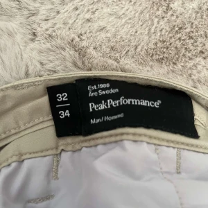 Beiga chinos från Peak Performance - Snygga beiga chinos från Peak Performance med raka ben och klassisk passform. Byxorna har bälteshällor, två bakfickor med diskret logga och är tillverkade i mjuk bomull. Perfekta för en clean och stilren look.
