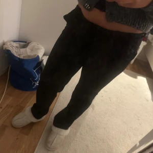 Svarta kostymbyxor från Vero Moda - Svarta kostymbyxor från Vero Moda med klassisk rak passform och midja med hällor. Byxorna har diskreta fickor och stängs med dragkedja och knapp. Perfekta till en snygg stickad tröja eller skjorta.