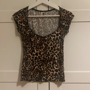 Leopardmönstrad topp från Nelly - Säljer en snygg leopardmönstrad topp från Nelly i storlek S. Toppen har korta ärmar, djup rundringning med svart spetskant och är figurnära i modellen. Materialet är mjukt och stretchigt, perfekt för att sticka ut lite extra.