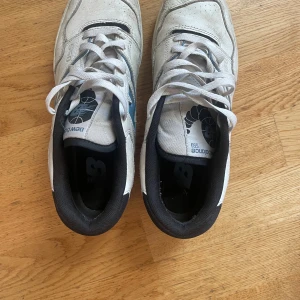 New Balance 550 vita sneakers strl 43 - Säljer ett par New Balance 550 sneakers i vitt med blå och svarta detaljer. Klassisk retrodesign med snörning, rund tå och platt sula. Ovandel i skinn och textil, sula i gummi. Perfekta för dig som gillar streetwear och sportig stil.