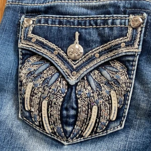 Miss Me jeans med broderad ficka, strl 25 - Snygga blå Miss Me jeans med broderad bakficka dekorerad med paljetter och detaljer i silver. Dom ör i bra skick, absolut inga bubbliga ställen på dom och alla knappar finns. Dom är bootcut och lite fade från blå till ljusblå, med lite glimmer på bakfickorna. 