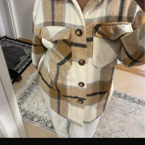 Rutig overshirt i beige och brunt - Snygg overshirt med stora rutor i beige, brunt och svart. Jackan har knappar framtill, två bröstfickor med lock och klassisk krage. Perfekt lager-på-lager-plagg för dig som gillar en avslappnad stil.