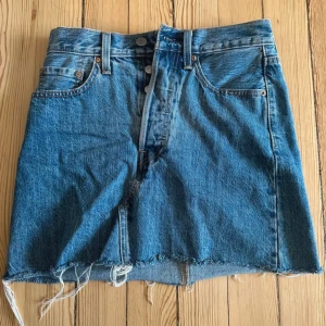 Levi's jeanskjol med rå kant - Snygg jeanskjol från Levi's med rå, fransig kant nertill. Kjolen har knappgylf. Endast använd fåtal gånger 🦋 Storlek 24.